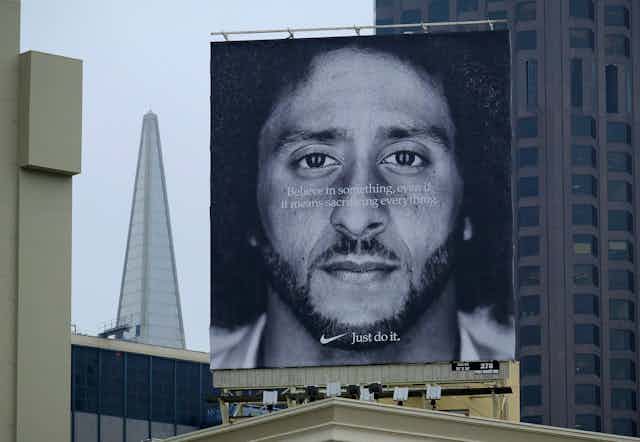 A large billboard featuring a quote that says 'Believe in something, even if it means sacrificing everything' superimposed over a black-and-white portrait of a Black man