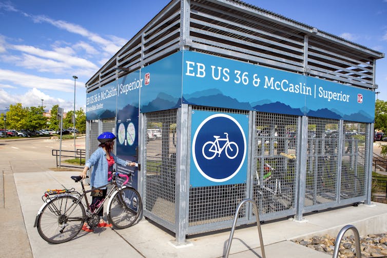 A woman enters metal enclosure to lock her bicycle.