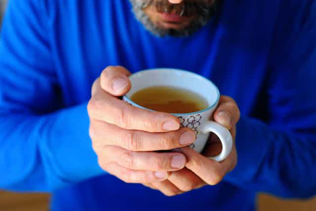 Un homme barbu tient dans ses mains une tasse contenant un liquide doré