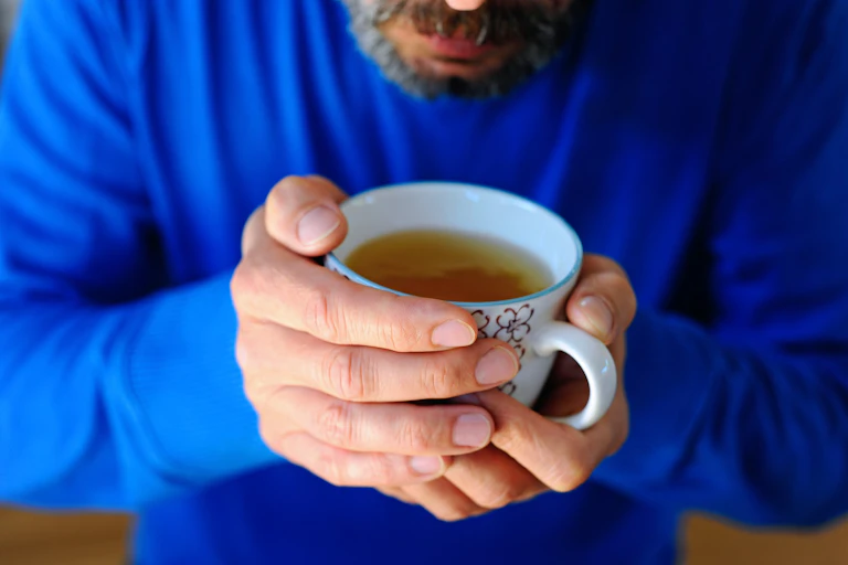 Un homme barbu tient dans ses mains une tasse contenant un liquide doré