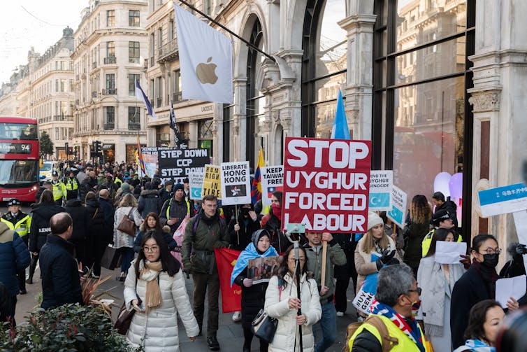 protesters march in streets holding signs in front of apple logo on a building