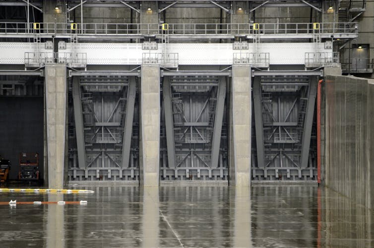 Three huge, closed metal gates reflected off wet pavement below.