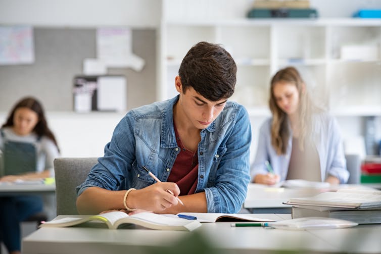 Three students work at desks in a classroom.