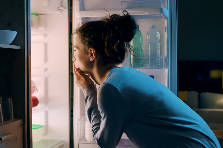 Woman looks in the fridge at night