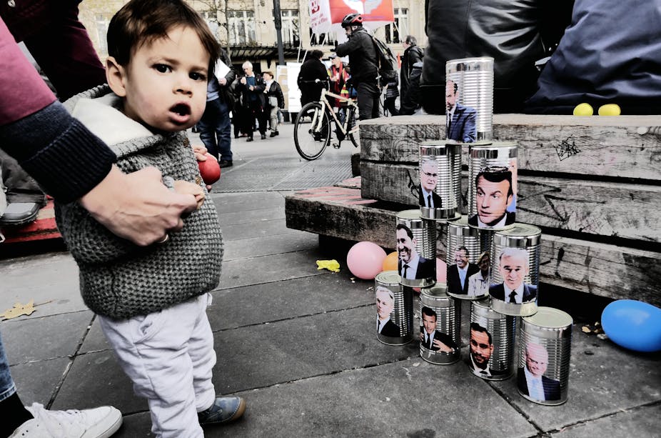 Un enfant devant une culbute de boîtes de conserve à l'effigie d'hommes politiques.