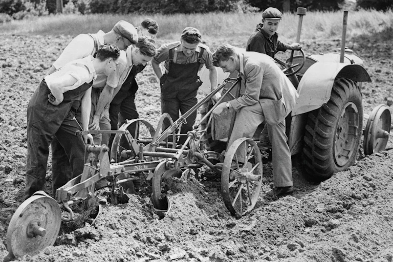 Group of men inspect a plough behind a tractor in a field