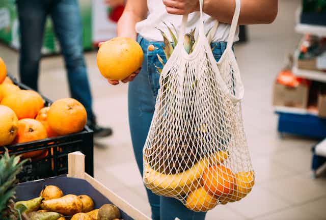 A woman fills a mesh netted shopping back with oranges and bananas
