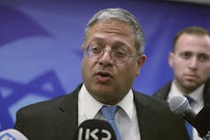 A grey-haired man in glasses speaks to the media.