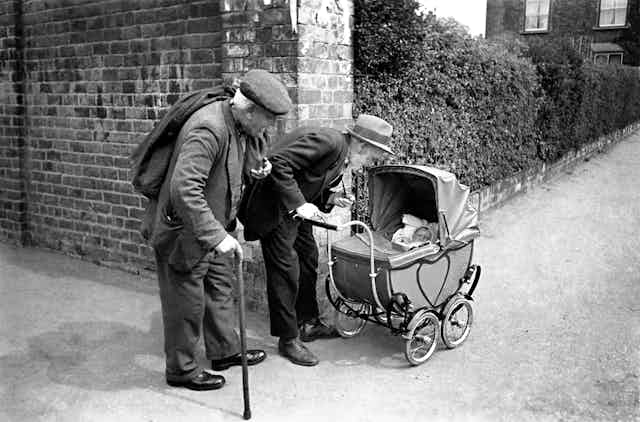An archival photograph of old men looking at a baby.