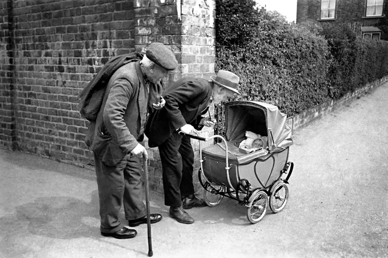 An archival photograph of old men looking at a baby.