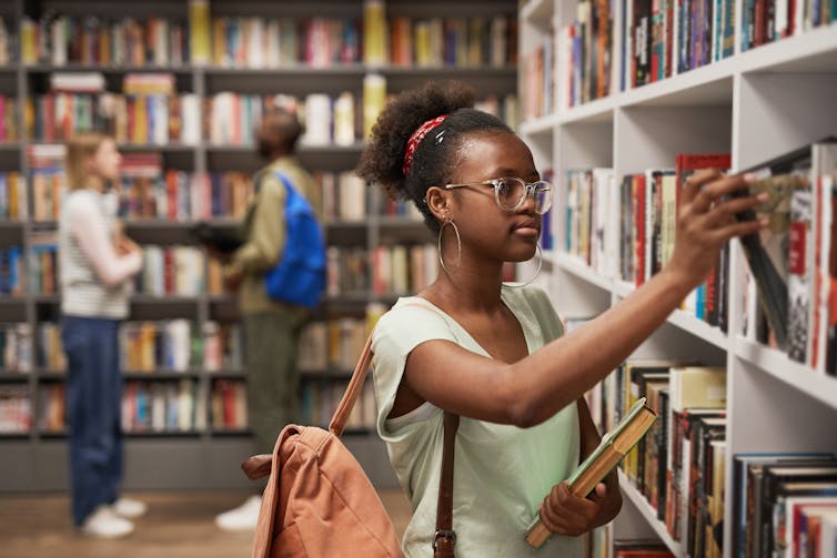 Black female student choosing a book in university library.