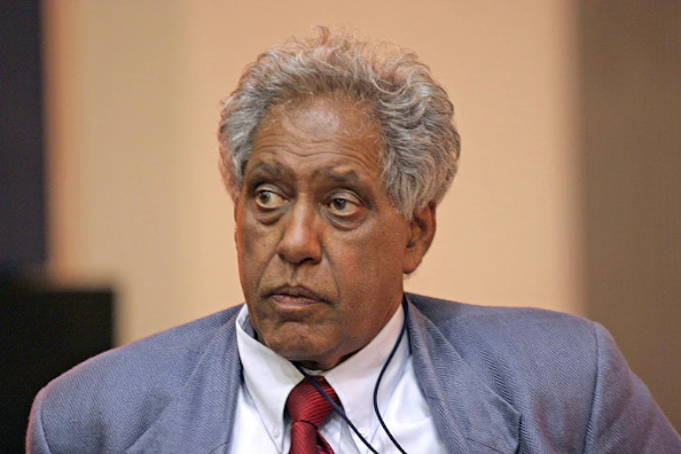 A serious-looking man wearing a jacket and tie stares into the distance.