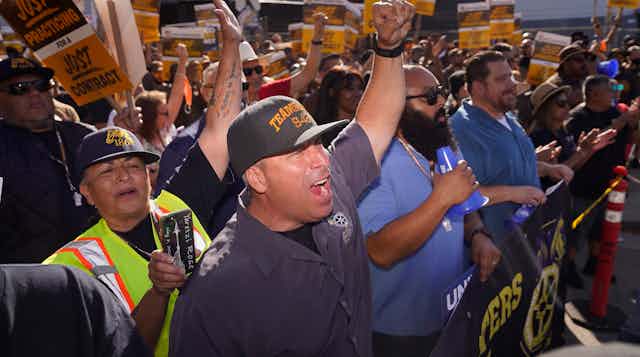 Workers, some holding UPS-branded signs that say 'just practicing' gather together to protest.