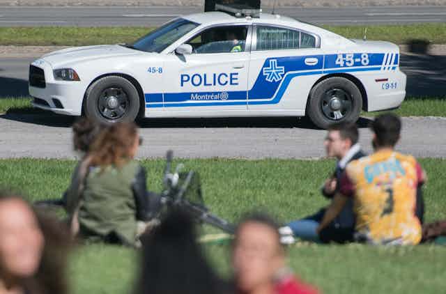 Une auto de la SPVM roule près de personnes assises dans un parc à Montréal.