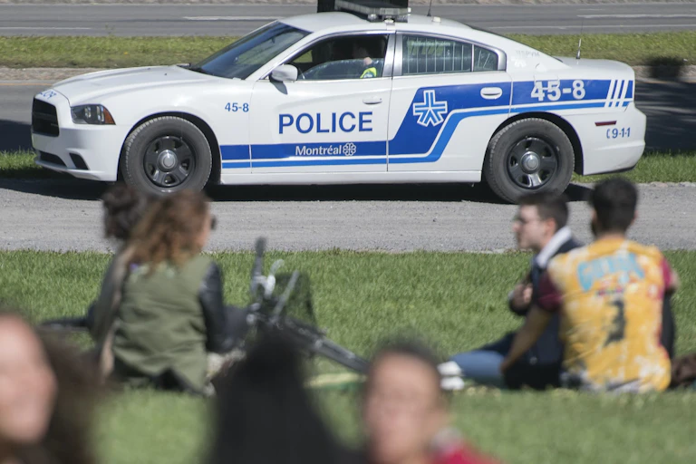 Une auto de la SPVM roule près de personnes assises dans un parc à Montréal.