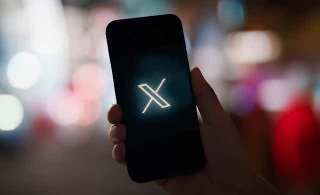 A hand holding a smartphone displaying the x logo