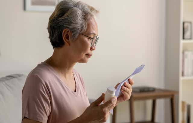 Older woman holds medicine bottle and looks at paper