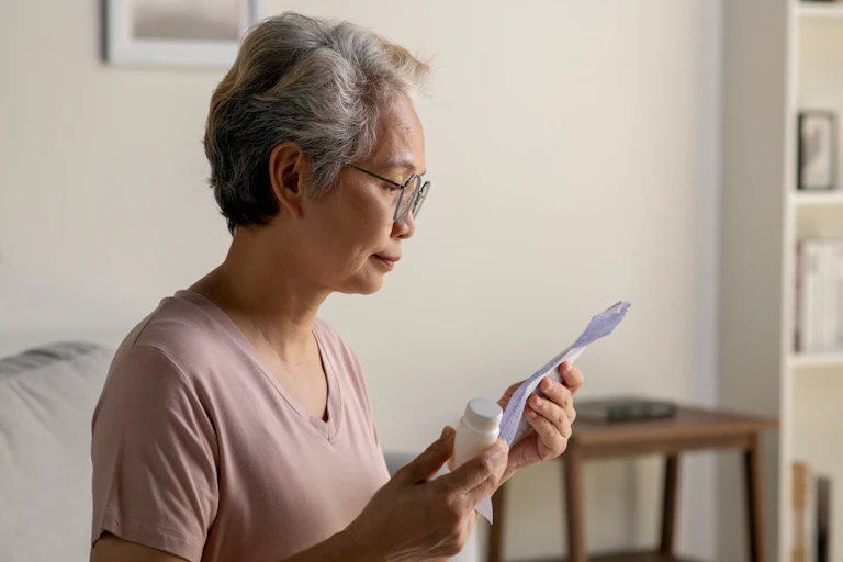 Older woman holds medicine bottle and looks at paper