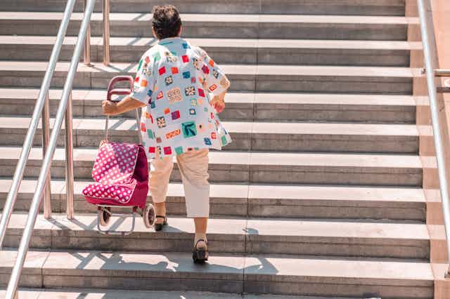 person on bright shirt carries shopping cart up stairs