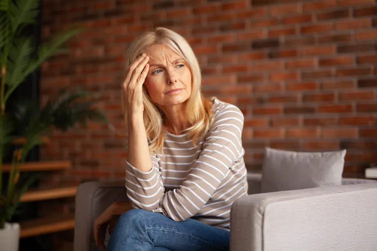 A woman sitting on a couch with a hand on her forehead.