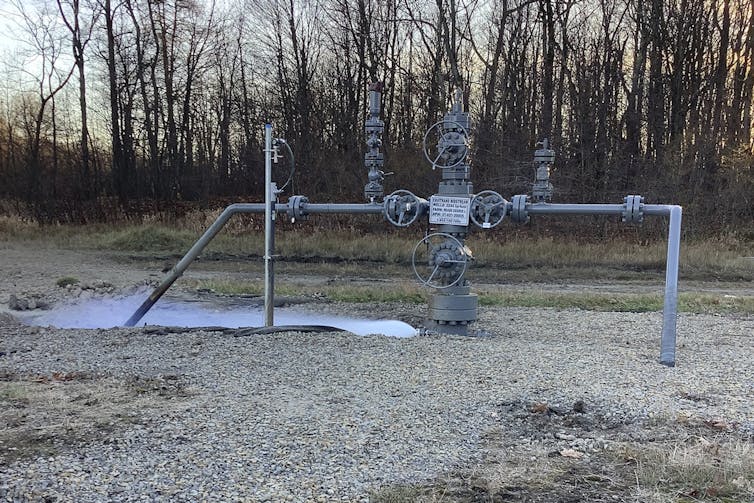 Methane leaks from a well in front of a line of trees.