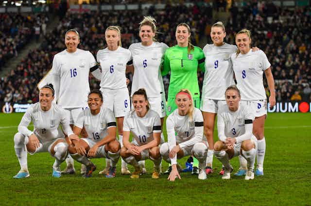 The England women's football team posing for a photo on the pitch.