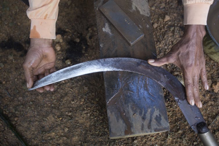A worker sharpens the blade of a sickle.
