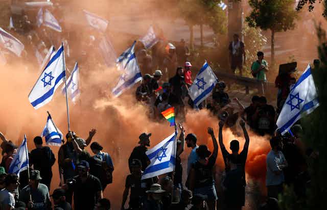 Israeli citizens in mass protests carrying national flags.