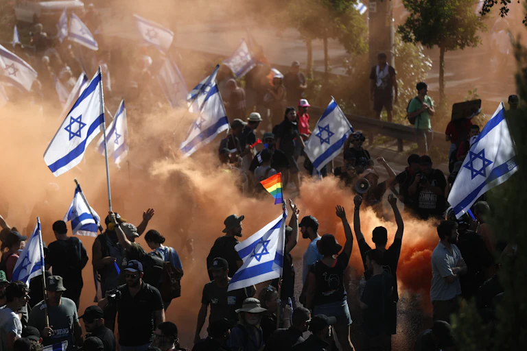 Israeli citizens in mass protests carrying national flags.