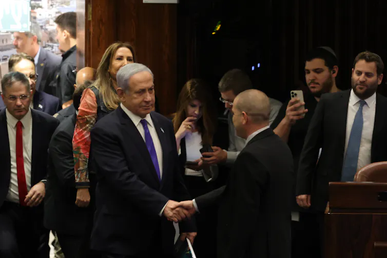 Israel's prime minister, Benjamin Netanyahu in the Israeli parliament hakes hands with a colleague while other MPs look on.
