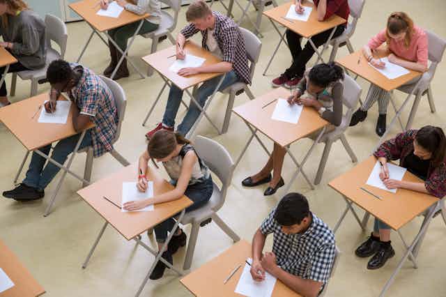 A large group of students in a classroom take a test. 
