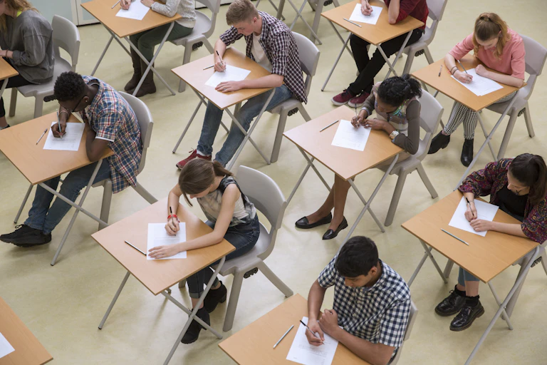 A large group of students in a classroom take a test.
