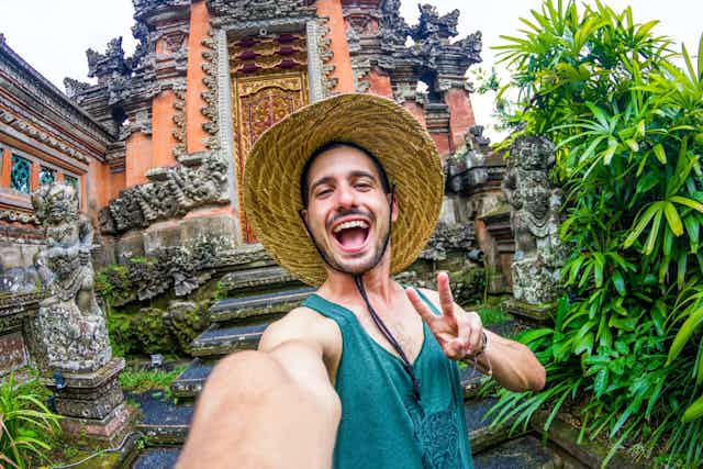 Un touriste avec un chapeau en paille prend un selfie devant un monument durant ses vacances. à Bali