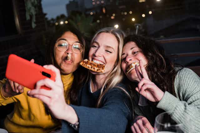 Multiracial girls having fun together outdoors in restaurant while taking selfie with smartphone - Main focus on central girl face.