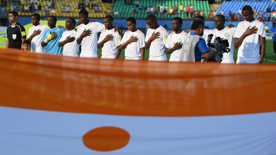 Des garçons debout en rang derrière le drapeau du Niger