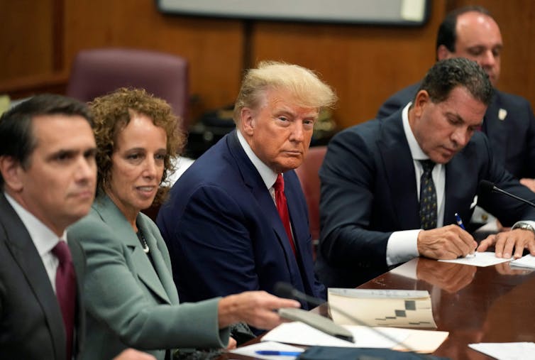 Cinco personas sentadas a un lado de una mesa con papeles sobre la mesa frente a ellos.