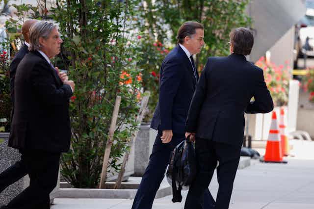 Three suited men, one holding a briefcase, walk toward a building.