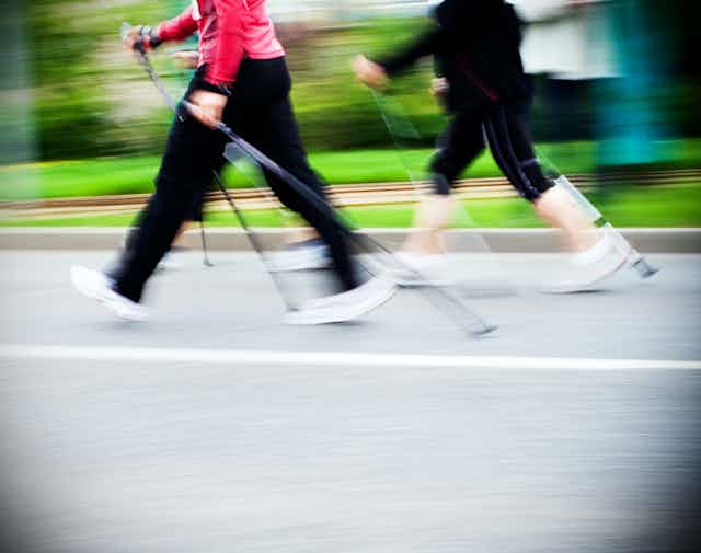 Deux personnes habillées en tenues de sport marchent avec des bâtons sur un chemin.