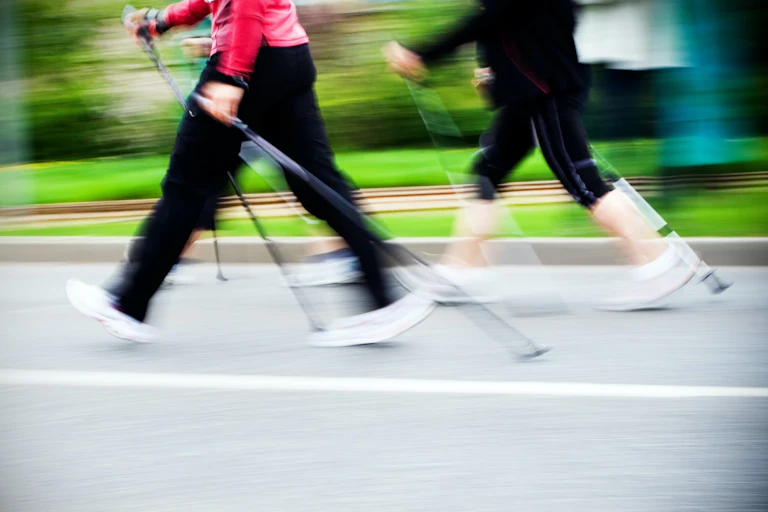 Deux personnes habillées en tenues de sport marchent avec des bâtons sur un chemin.