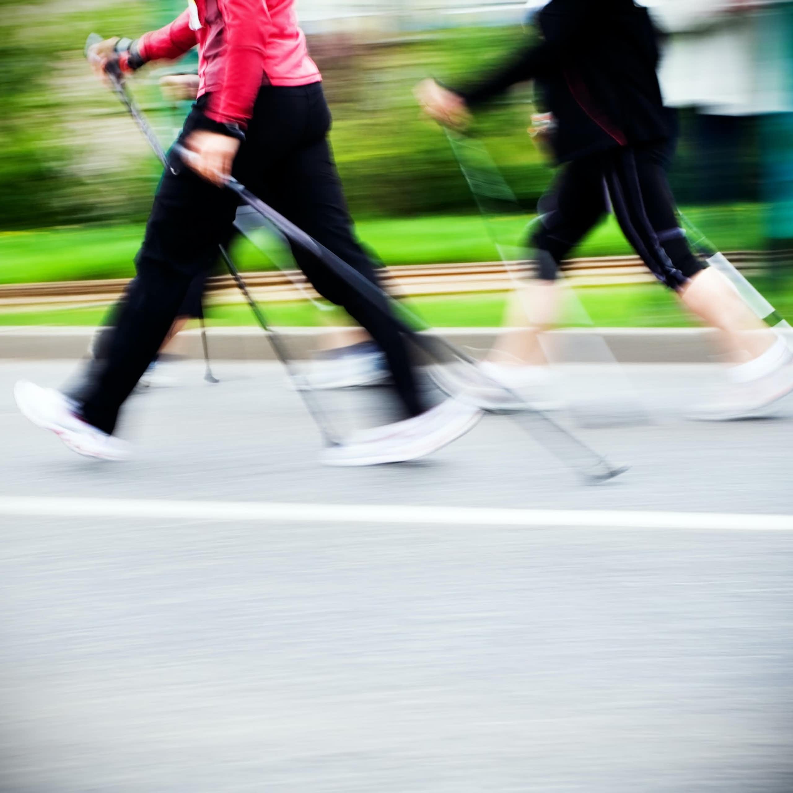 Deux personnes habillées en tenues de sport marchent avec des bâtons sur un chemin.