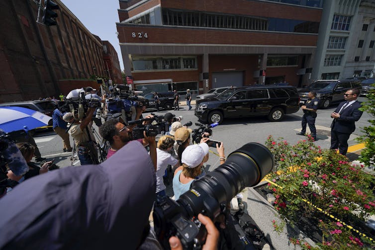 A group of people with cameras in a parking lot near a number of office buildings.