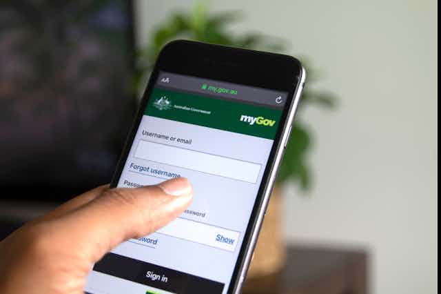 A photo of a person holding a phone showing the myGov website.