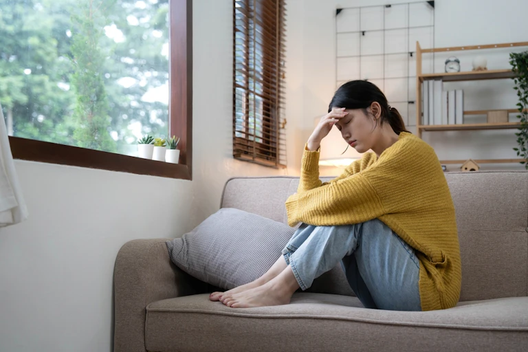Young woman, legs up on sofa, holding head with one hand