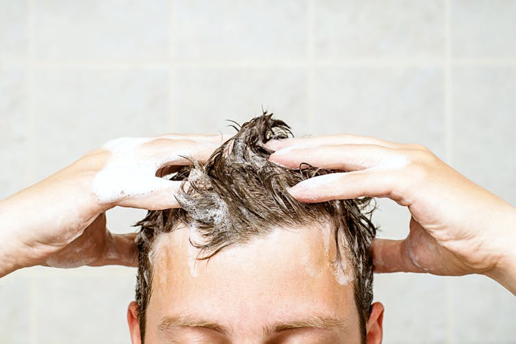 Man washing hair in shower, dark hair with shampoo suds