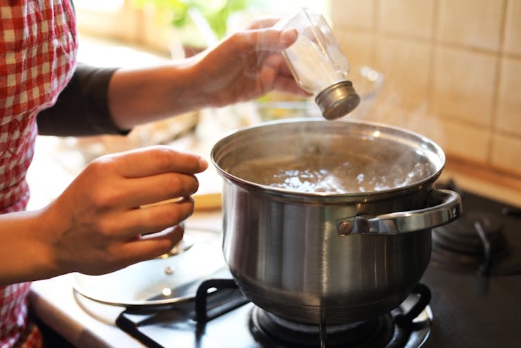 Woman adding salt to pot of boiling water on stove