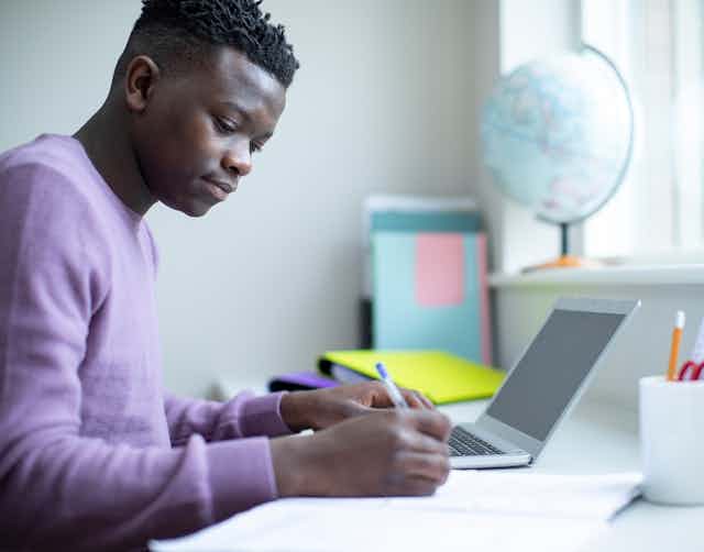 Teenage boy doing homework with laptop open