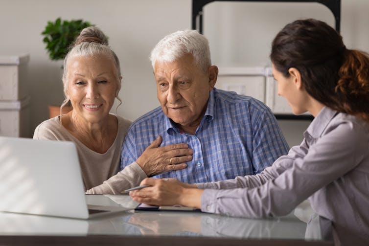 Man and woman in front of a laptop with another woman speaking to them.