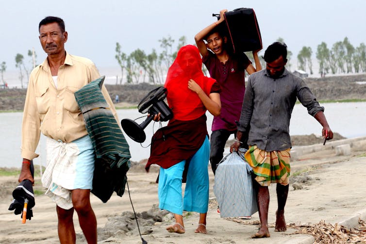 People walk along a waterway with their belongings.