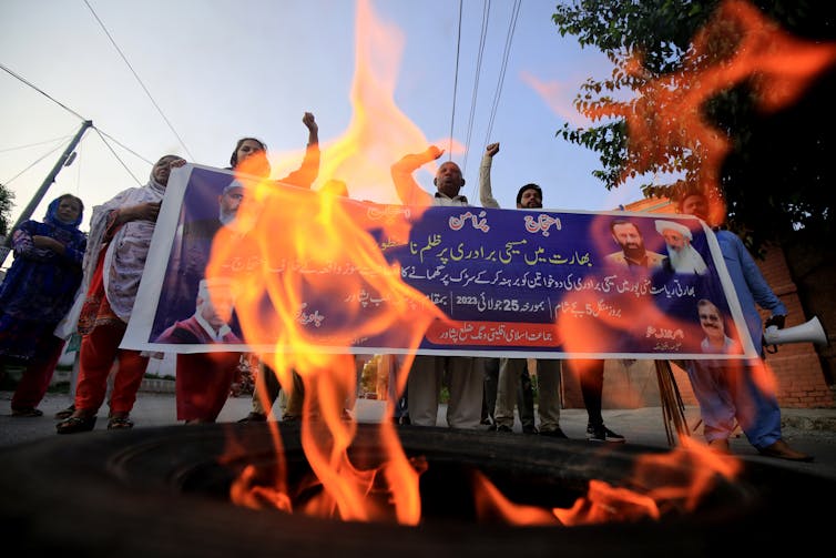 Flames in front of protesters holding placards protesting about sexual violence against women.