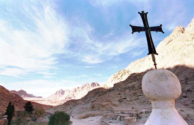 A cross resting on top of a monastery located amid mountains.
